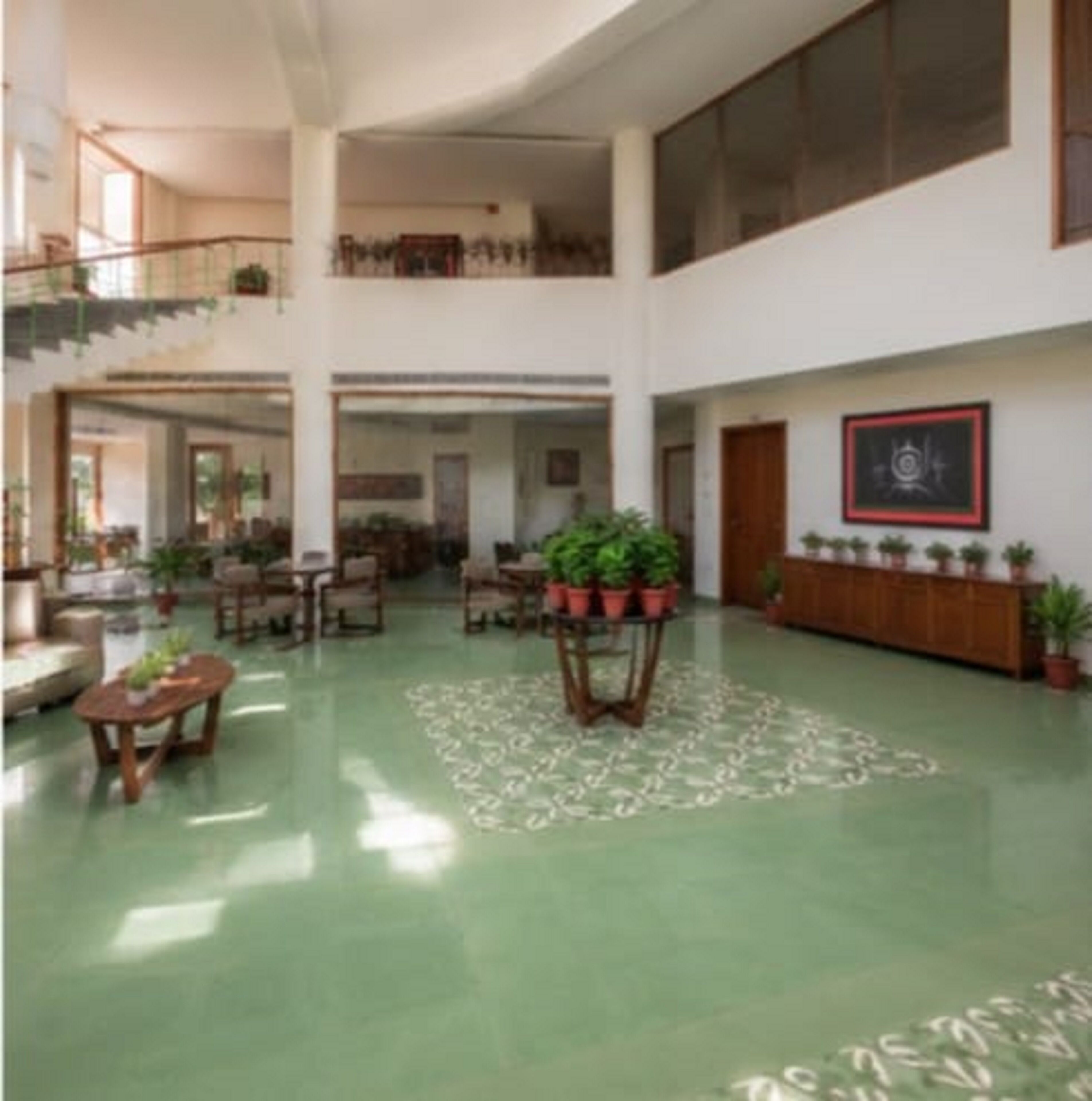 A spacious lobby with a green floor, wooden furniture, and potted plants.