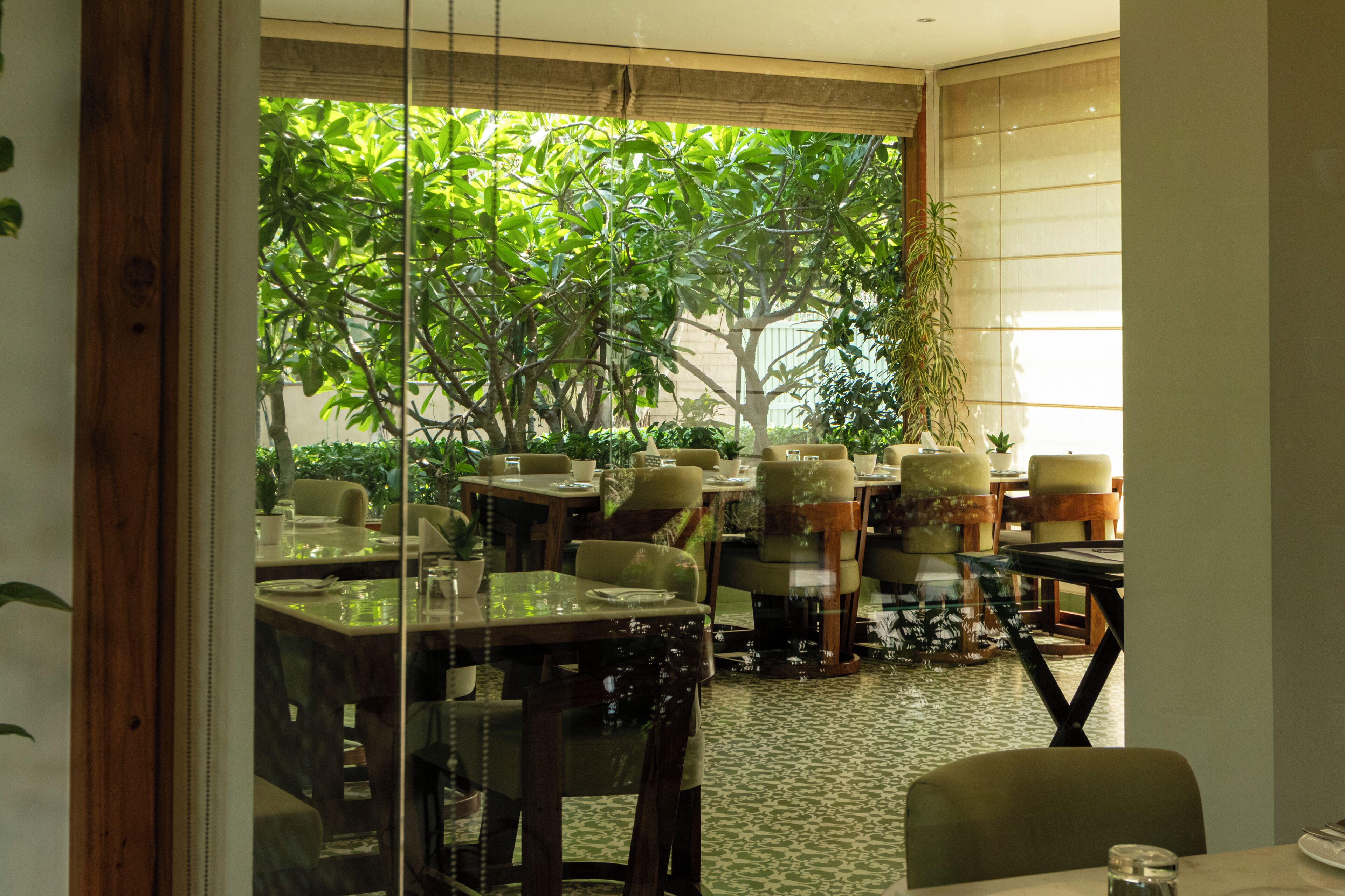 An indoor dining area with tables and chairs, a view of greenery outside, and a patterned floor.