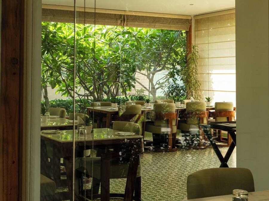 An indoor dining area with tables and chairs, a view of greenery outside, and a patterned floor.