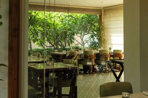 An indoor dining area with tables and chairs, a view of greenery outside, and a patterned floor. - Naad Wellness (Sonepat)