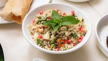 A bowl of couscous salad with vegetables and pomegranate seeds, garnished with mint leaves.