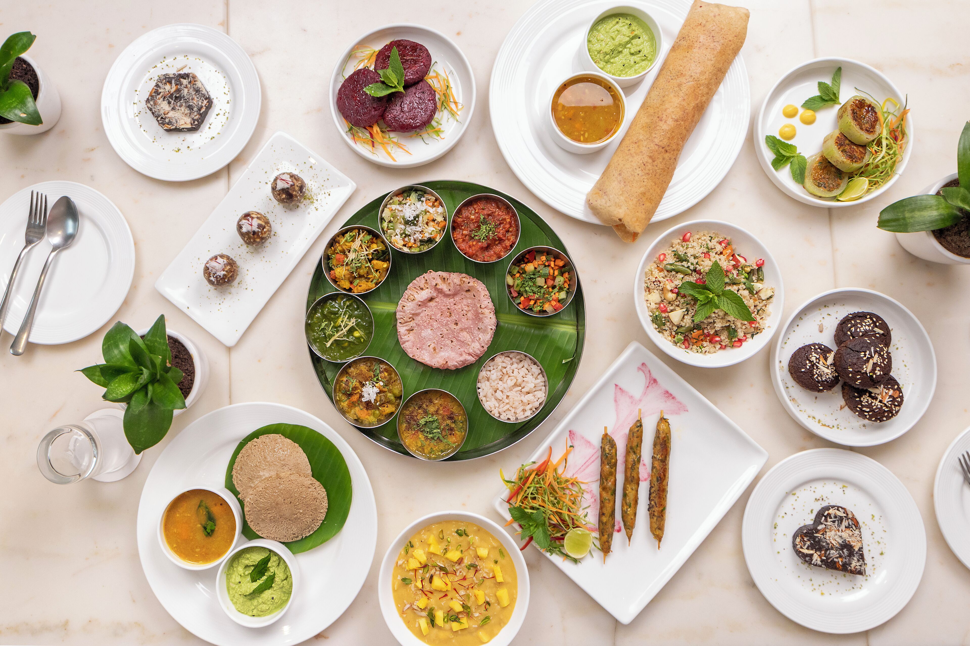 Une variété de plats présent és sur plusieurs assiettes et sur une feuille de bananier, ce qui témoigne d’un choix de mets diversifié.