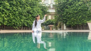 A person sitting by a clear pool with trees in the background. - Naad Wellness (Sonepat)