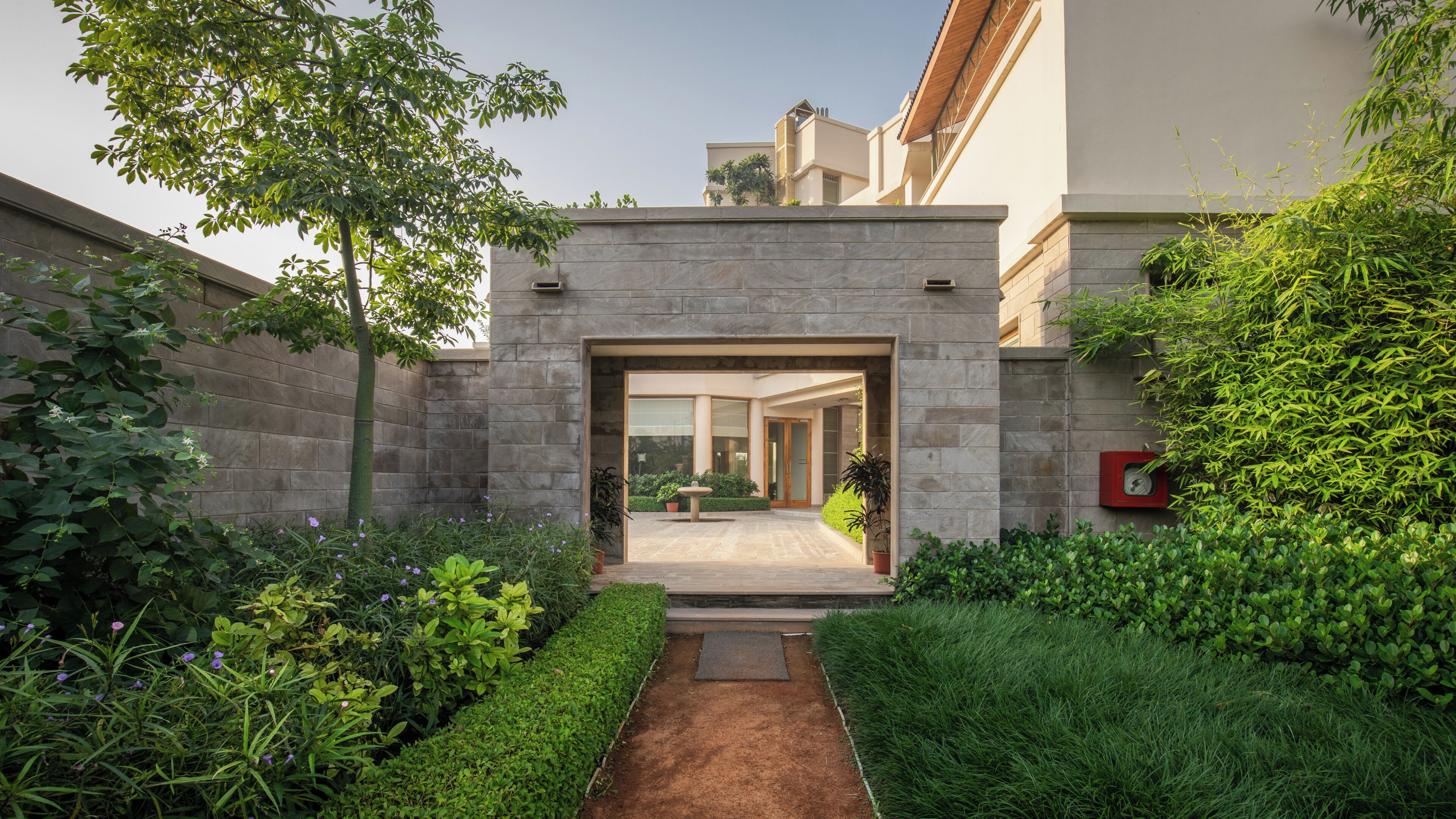 Ein modernes Gebäude mit Steinaußenwand, befestigtem Eingangsbereich und einem Garten mit unterschiedlichen Pflanzen.