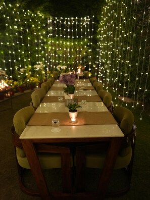 A long dining table with chairs, set with a candle, and surrounded by string lights. - Naad Wellness (Sonepat)