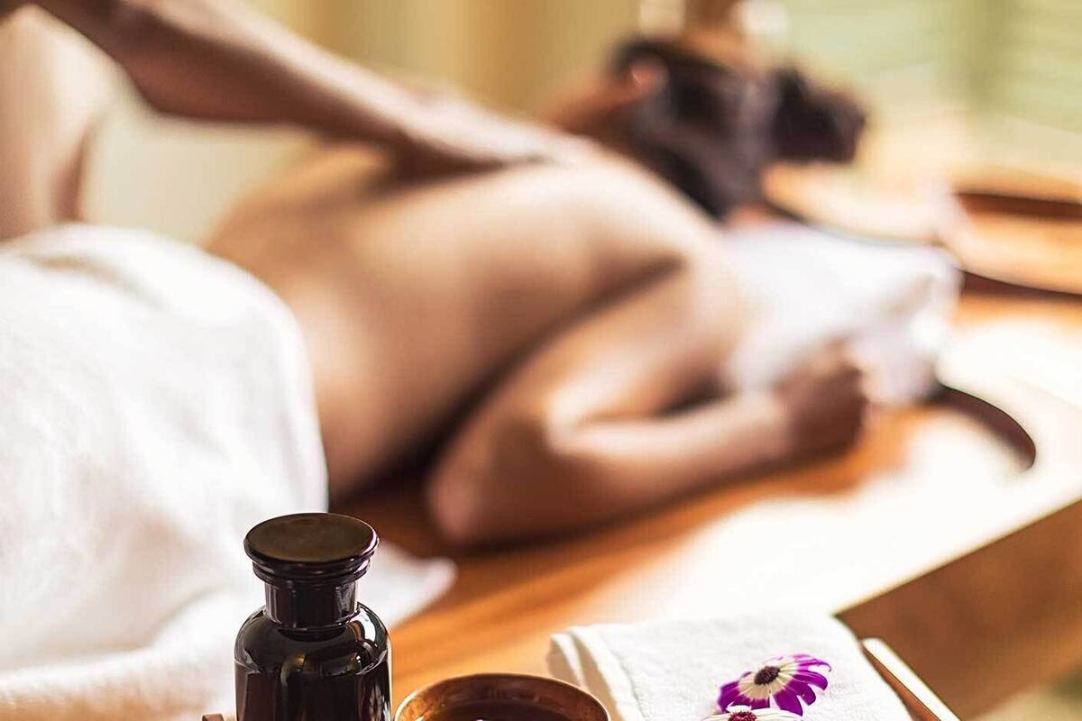 A spa setting with a massage table, a bottle of oil, and a flower on a tray.