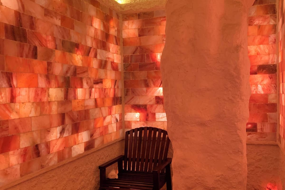 A spa room with a wooden chair, a large white pillar, and a wall of red and orange tiles.