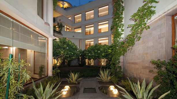 A courtyard with potted plants, a water feature, and a building with multiple windows. - Naad Wellness (Sonepat)