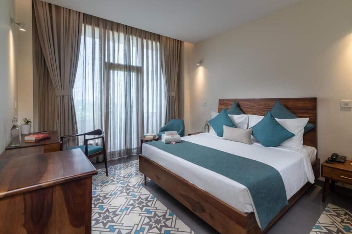 A hotel room with a bed, a desk, a chair, a nightstand, and a window with curtains.