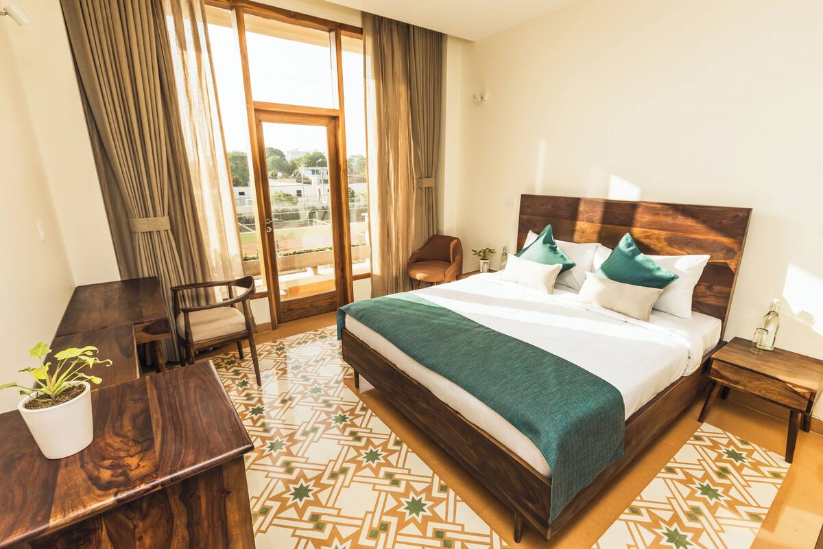 A hotel room with a large bed, a desk, a chair, and a view of the outdoors.