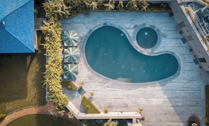 An aerial view of a swimming pool with a unique shape, surrounded by a stone deck and shaded by umbrellas. - Naad Wellness (Sonepat)