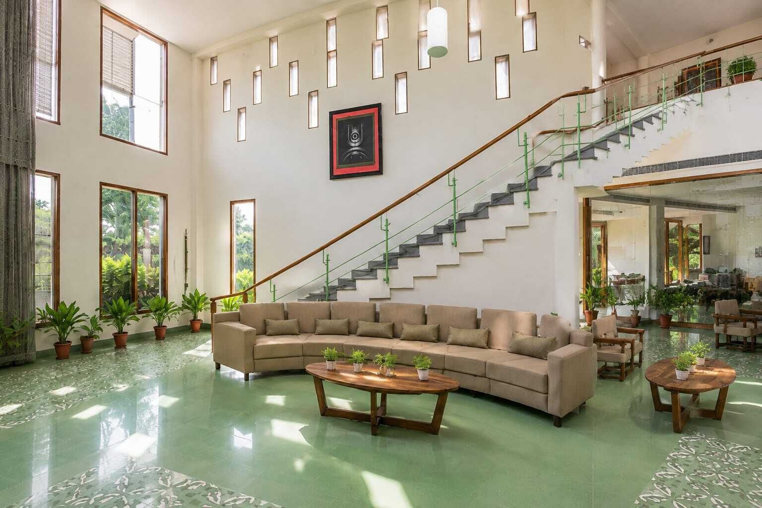 A spacious living area with a large beige sofa, a wooden coffee table, and a staircase with a green railing.