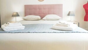 A neatly made bed with pillows, a folded towel, and a blanket on a bed with a pink headboard. There are two wall-mounted decorative plates above the bed. - Charmant Appartement au Pied D'un Parc Arboré (Clichy)