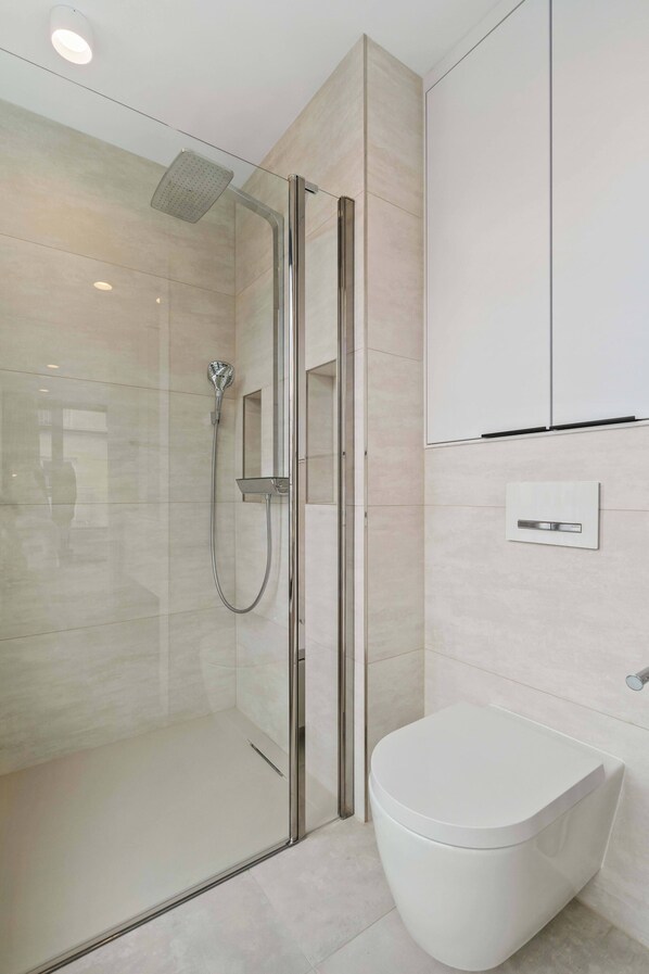 A modern bathroom with a glass-enclosed shower, a white toilet, and a wall-mounted sink.