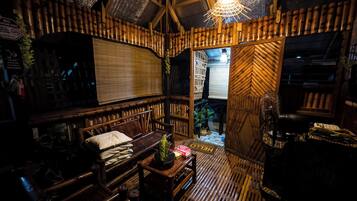 Una habitación con paredes y techo de madera, una banca, una mesa con una planta y un ventilador.