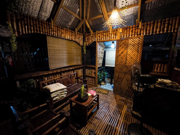 Una habitación con paredes y techo de madera, una banca, una mesa con una planta y un ventilador.