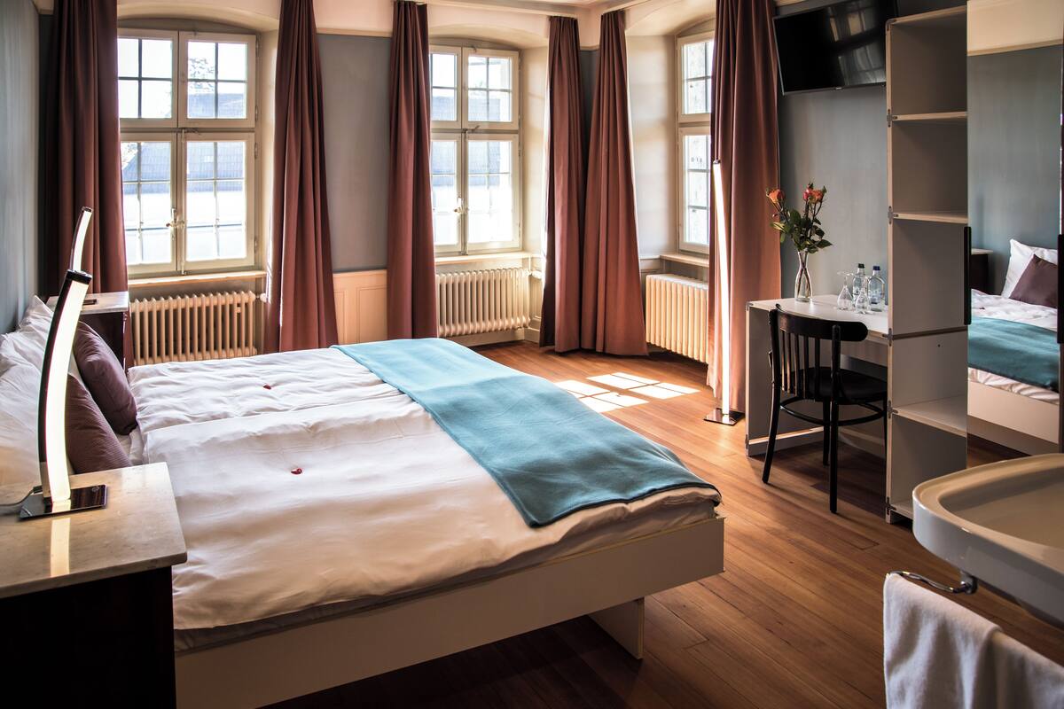 Een hotelkamer met een groot bed, een bureau, een stoel, een badkamer en een aan de muur bevestigde televisie.
