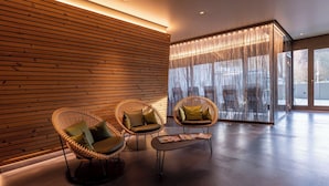 Un hall d’entrée moderne avec des panneaux de bois, des fauteuils en osier dotés de coussins, une cloison en verre et une grande fenêtre avec des rideaux.