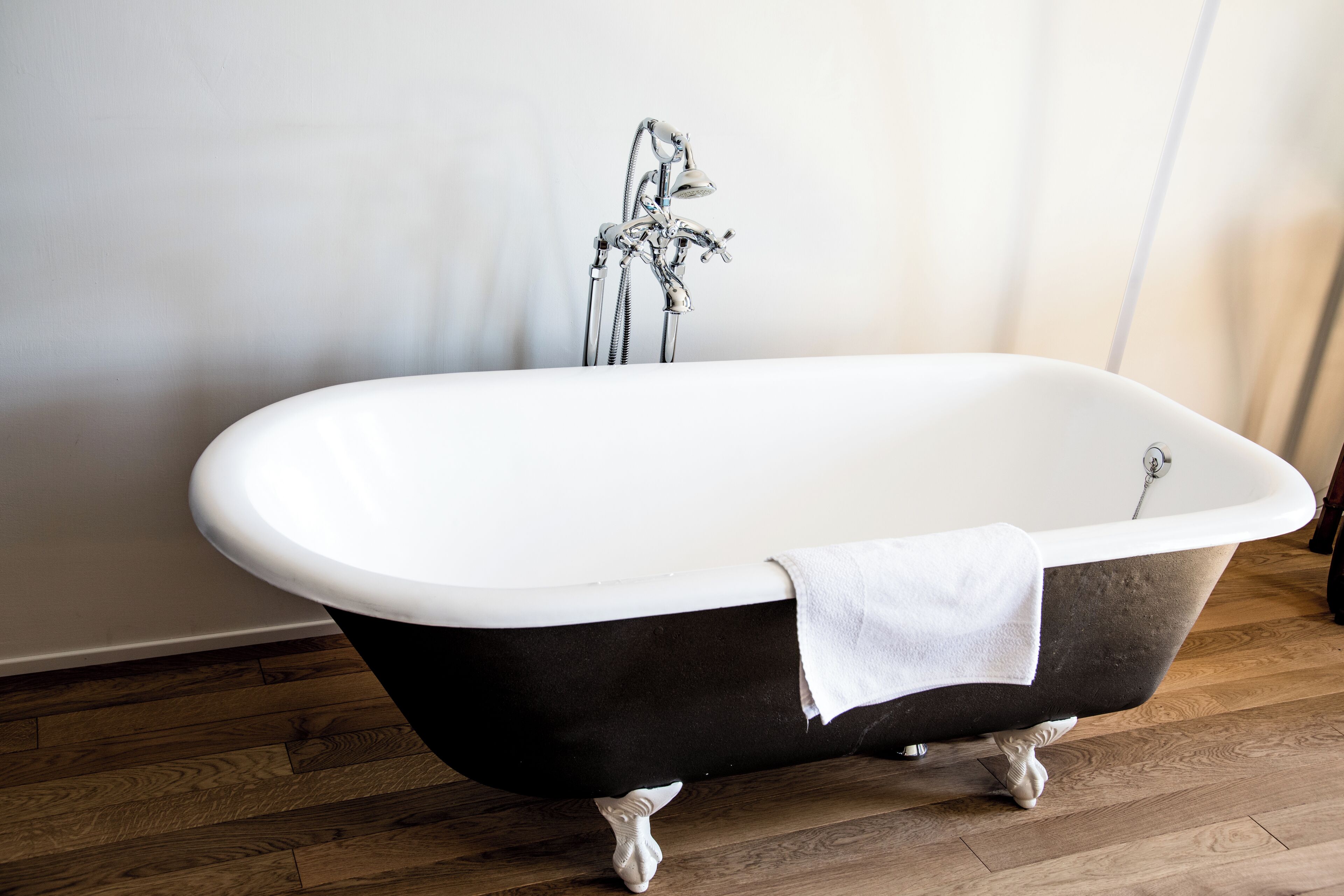 Una bañera independiente con una toalla blanca, suelo de madera y una pared lisa.