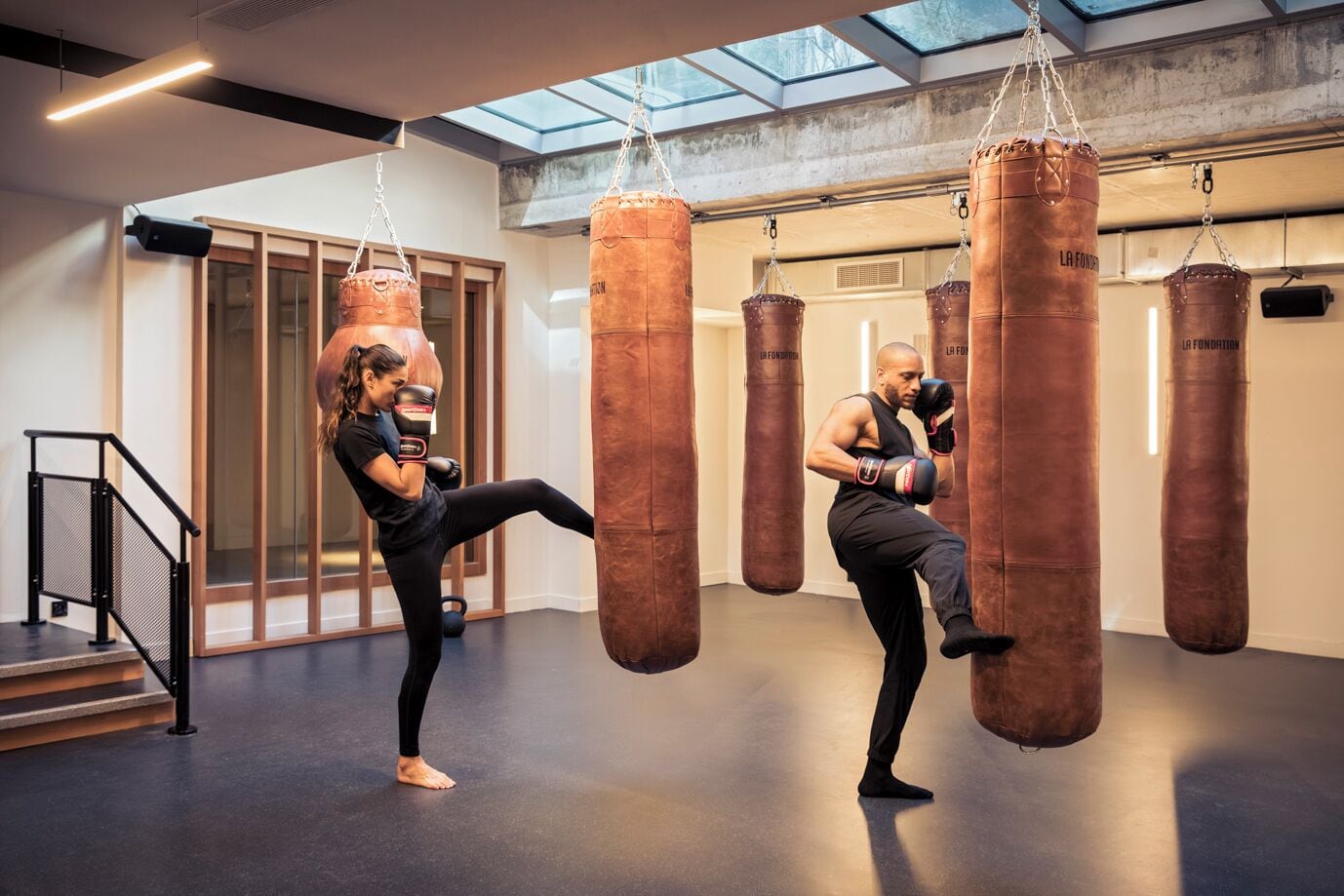 Un gimnàs amb dues persones fent kickboxing, equipat amb saques de boxa i una escala.