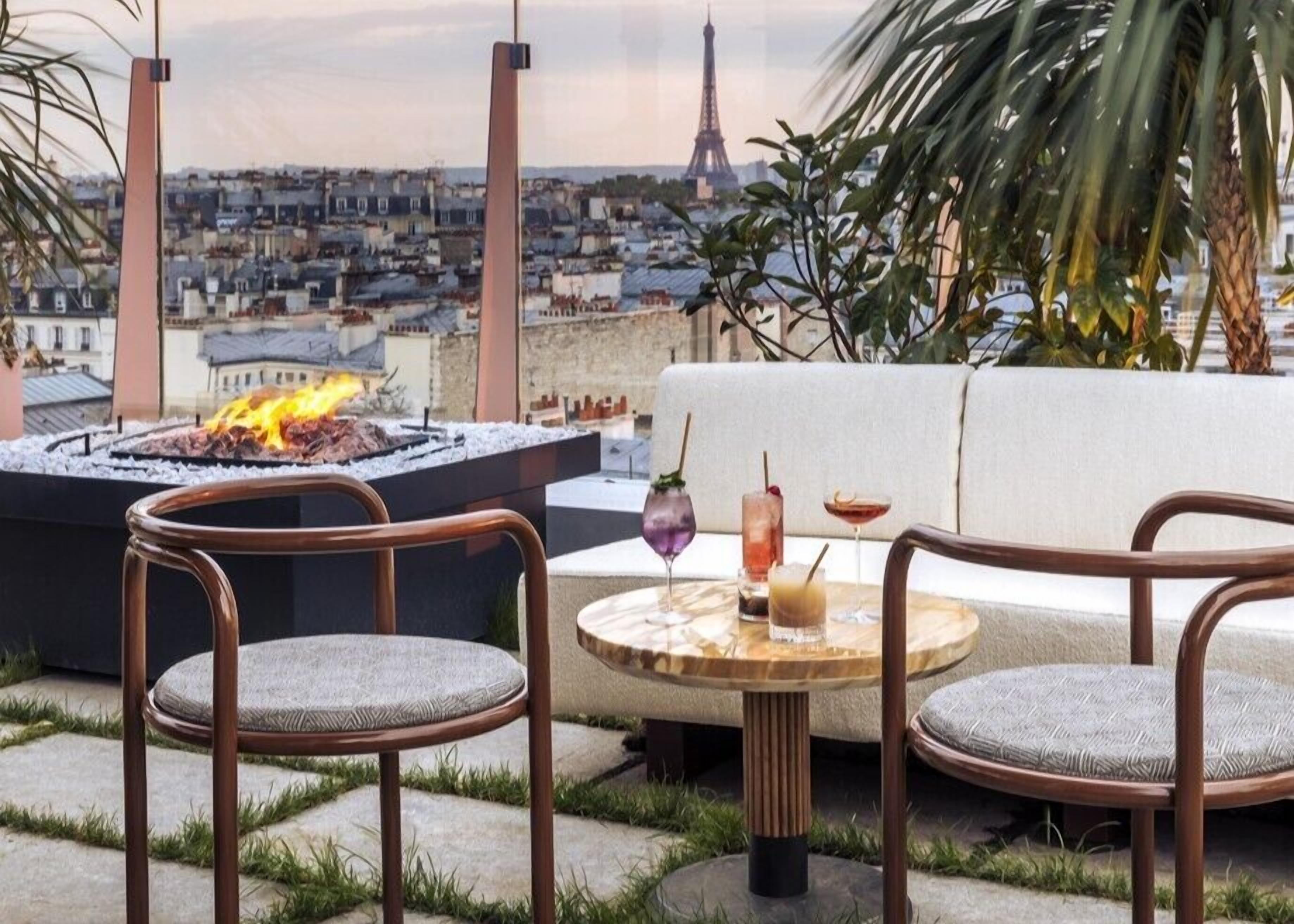 Une terrasse sur le toit avec un foyer, deux chaises, une table ronde avec des boissons et une vue sur la Tour Eiffel.