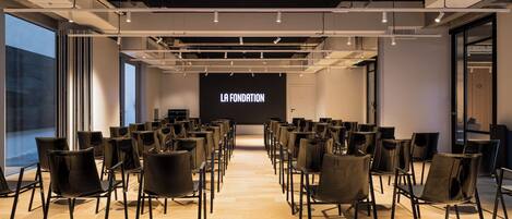 A conference room with rows of chairs facing a screen displaying "LA FONDATION".