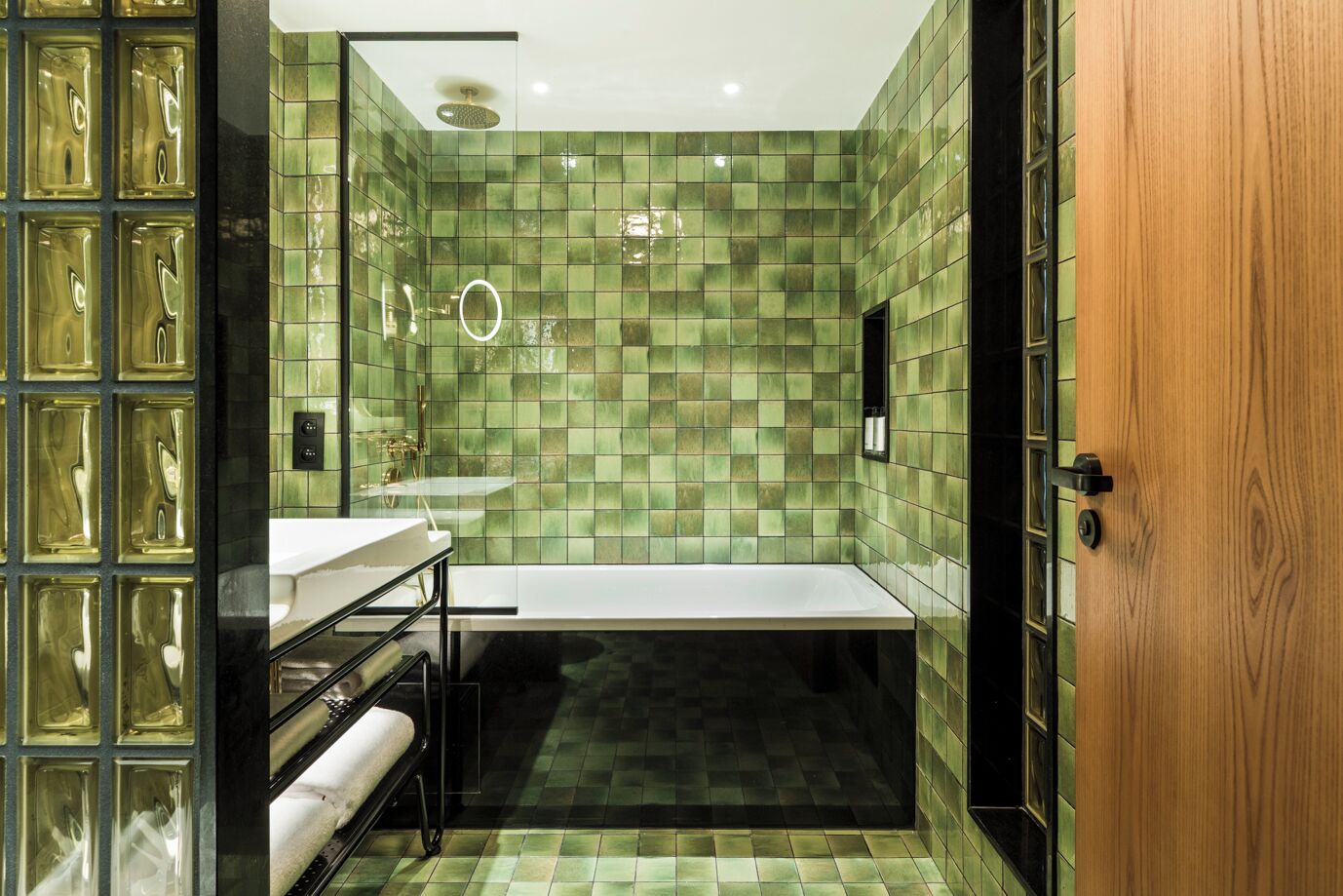 Un baño con mosaicos verdes, un lavamanos blanco, una bañera y una puerta de madera.