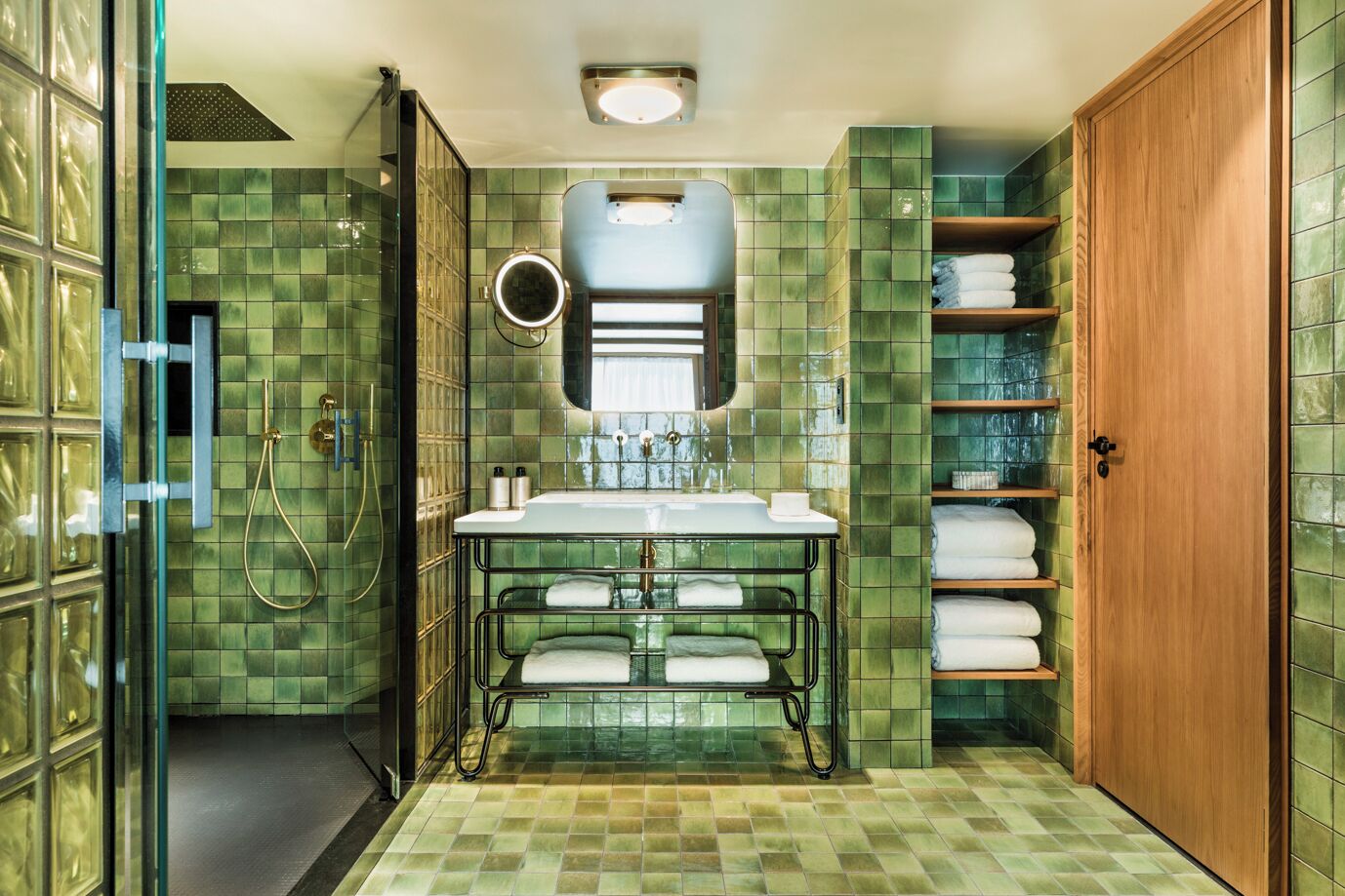 A bathroom with a glass shower enclosure, a sink with a mirror, and shelves with towels.