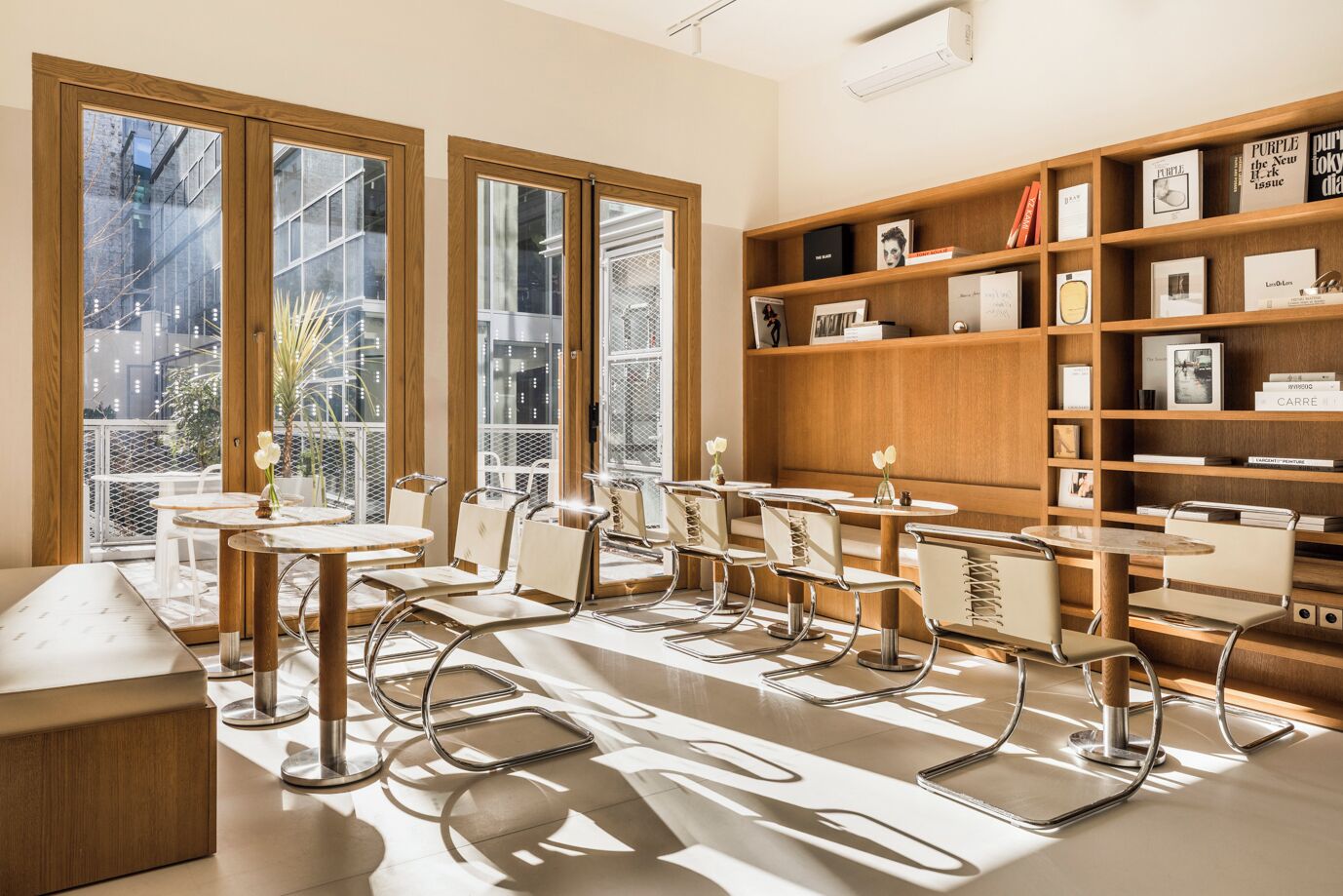 Un intérieur moderne avec de grandes fenêtres, une bibliothèque en bois et un espace salon avec des tables et des chaises.