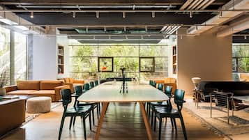 Une salle de réunion spacieuse, dotée d’une grande table et de chaises, entourée de sièges confortables et de larges fenêtres offrant une vue sur la verdure.