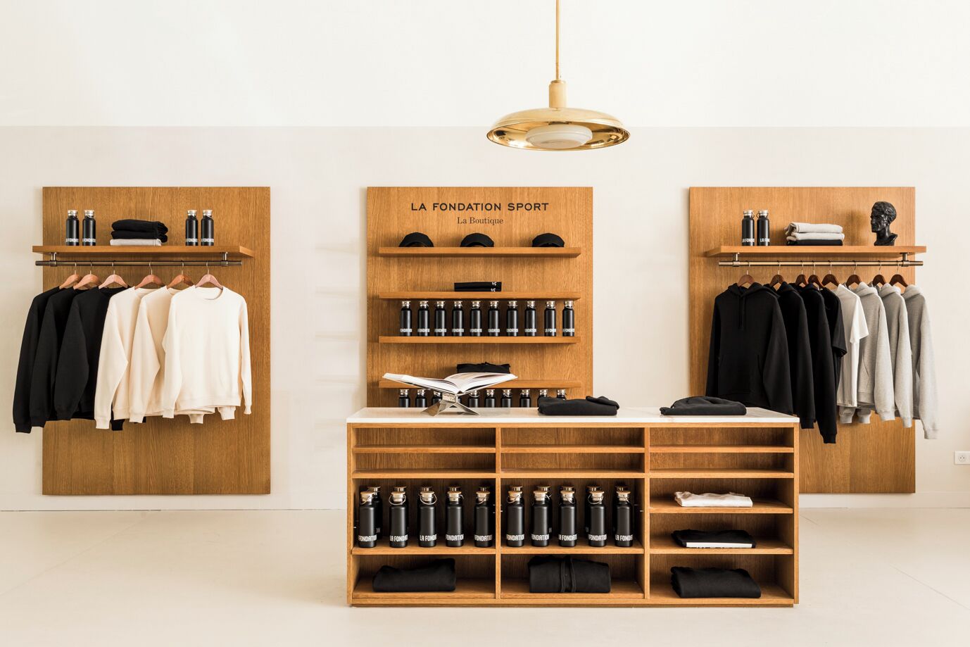 Un boutique moderno con estanterías de madera que exhiben ropa y accesorios, una mesa central con libros y una lámpara, y un diseño minimalista.
