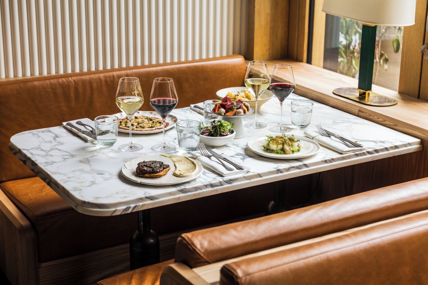 Une table à manger avec des assiettes remplies de nourriture, des verres de vin et des couverts.
