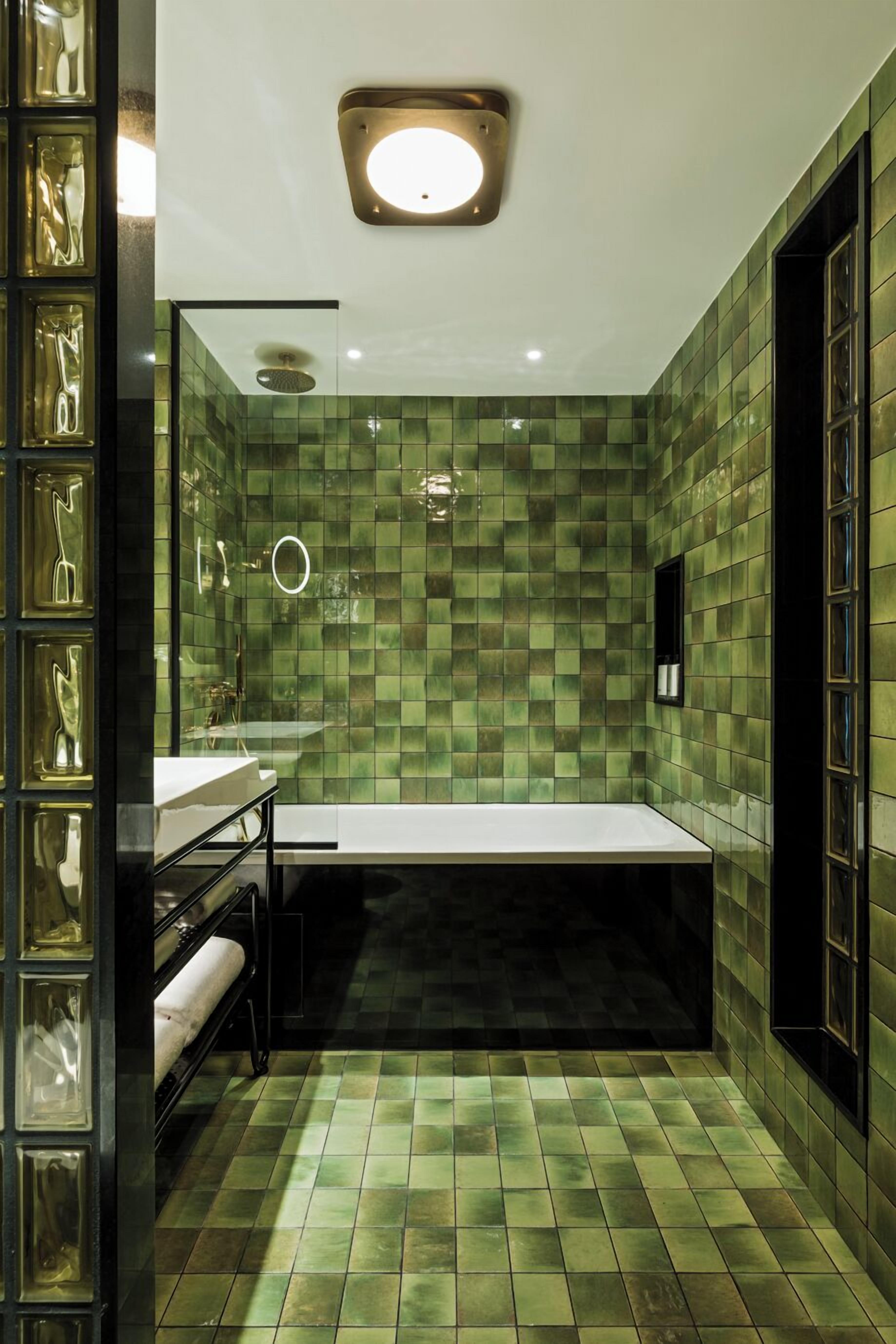 A bathroom with green mosaic tiles, a white sink, and a black towel rack.