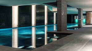 Une piscine intérieure moderne, dotée d’une eau cristalline, entourée de murs recouverts de carreaux foncés et agrémentée d’éléments de design minimalistes.