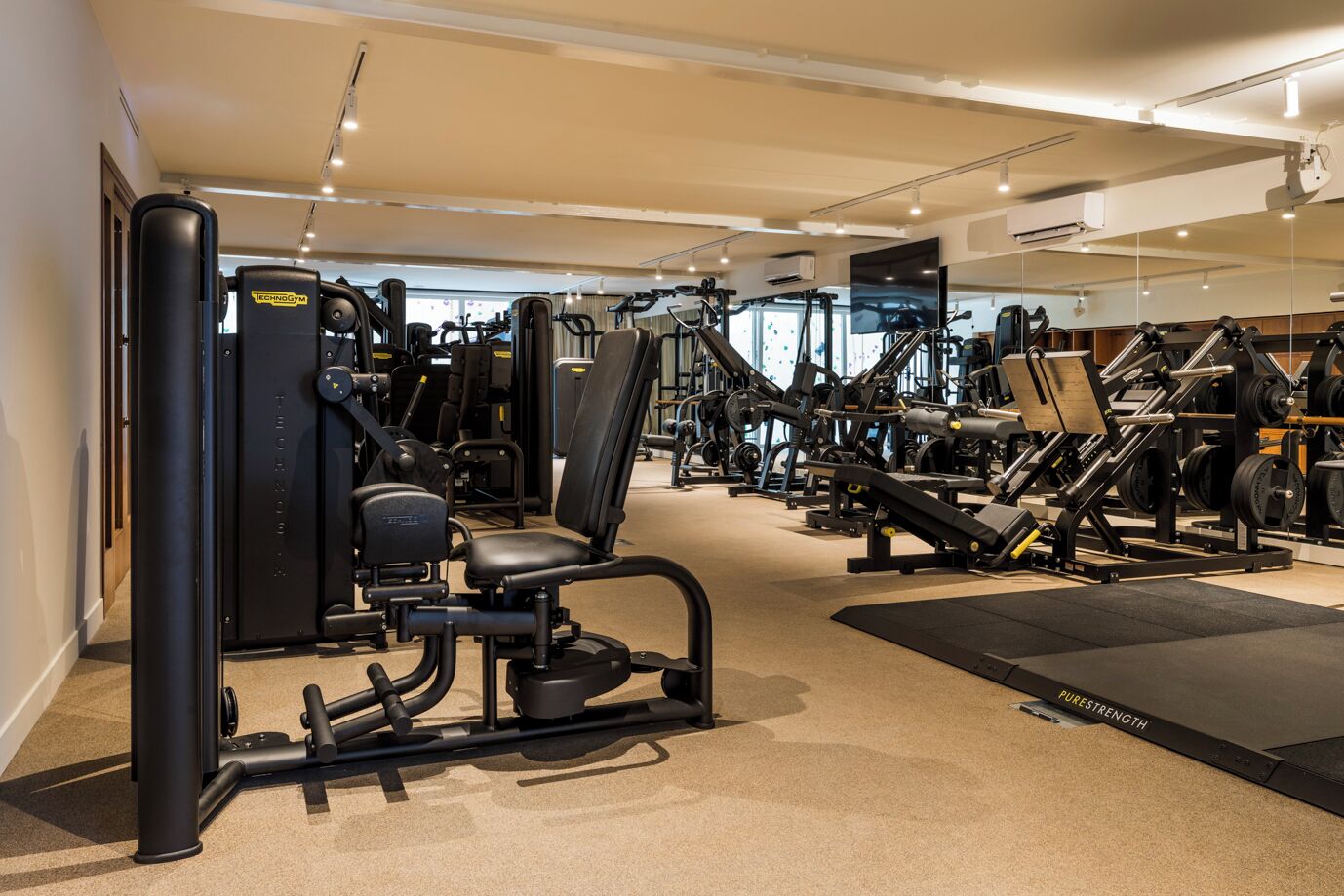 Un gimnasio bien equipado con diversas máquinas de ejercicio, una banca de pesas y un espejo.