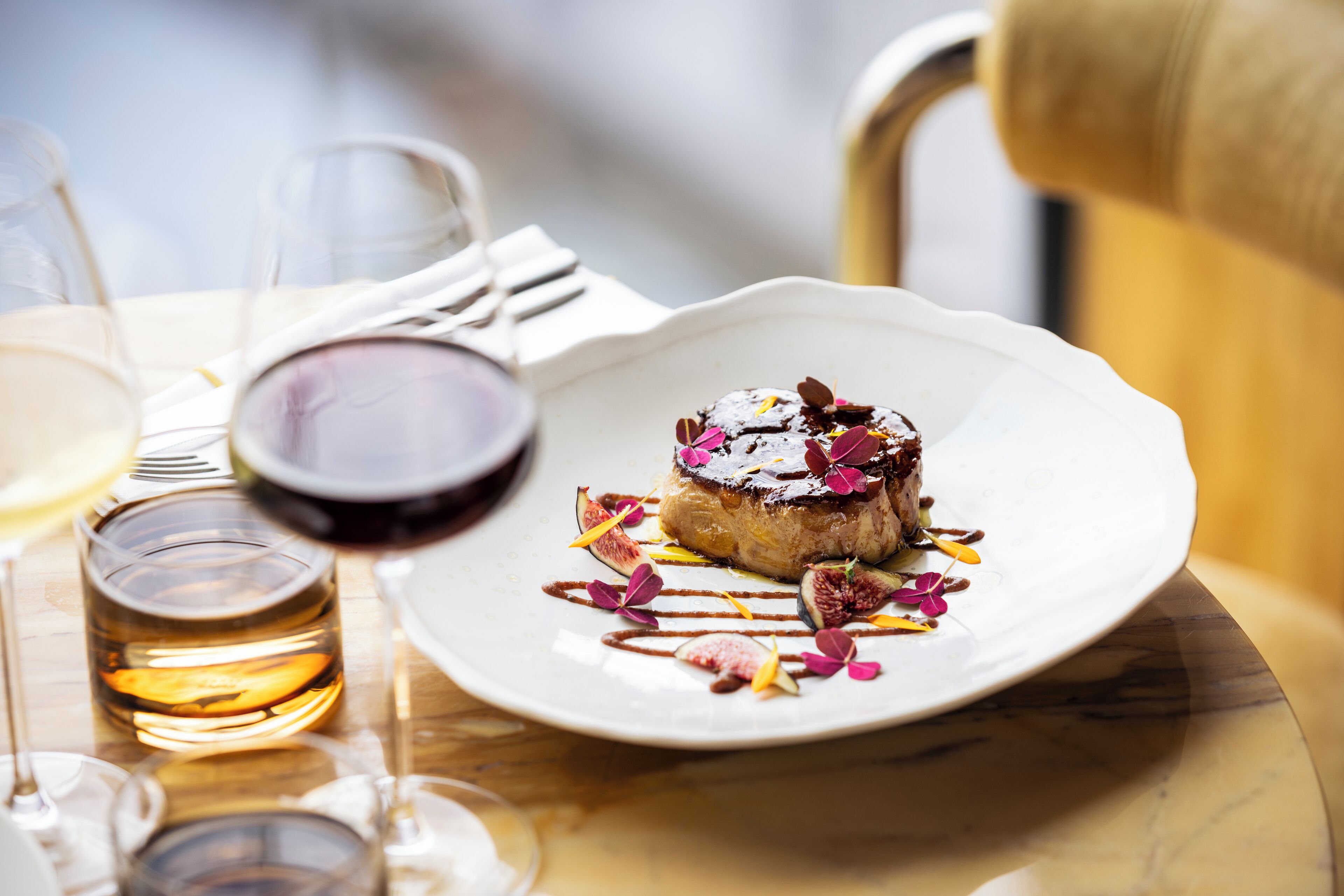 Un postre en un plato blanco, una copa de vino y una servilleta sobre una mesa.