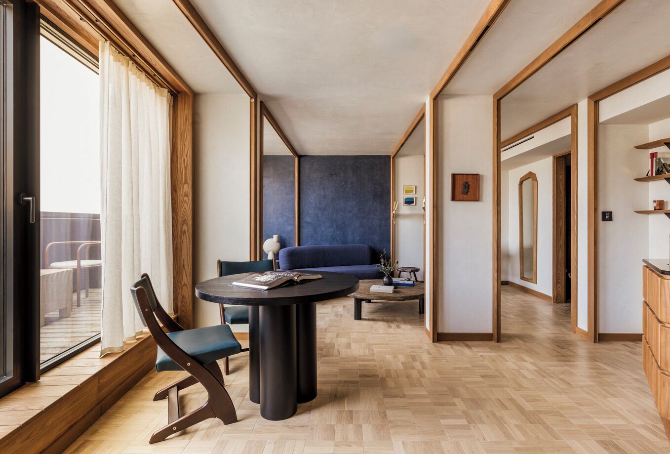 Un salon moderne avec une table ronde, un canapé bleu et une grande fenêtre avec des rideaux.