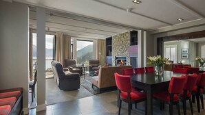 A spacious living room with a fireplace, a dining area with red chairs, and a balcony with a view of the mountains. - Stunning Villa Fabulous views over Queenstown (Queenstown)