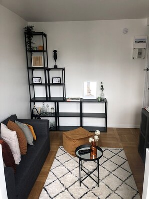 A living room with a dark sofa, a coffee table, a black shelving unit, and a patterned rug. - Studio Near Eiffel Tower JO 2024 (Paris)