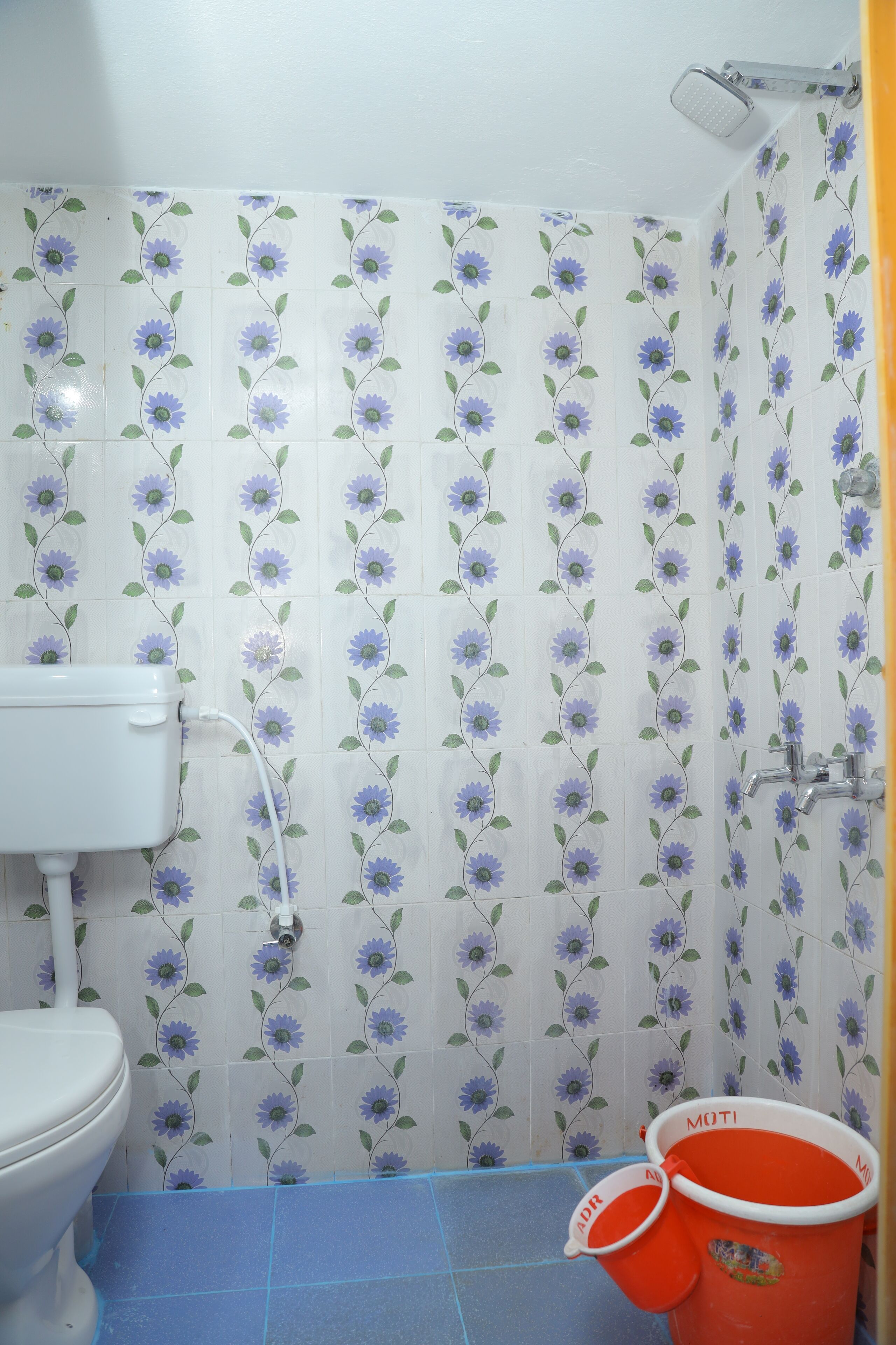 A bathroom with a toilet, shower, and two red buckets labeled "MOTI".
