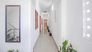 A long, narrow hallway with white walls, a mirrored wall on the left, and a sign indicating Room 6/7. - La Bell Residency Near Auroville Beach (Vanur)