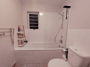 A bathroom with a bathtub, toilet, and a window.