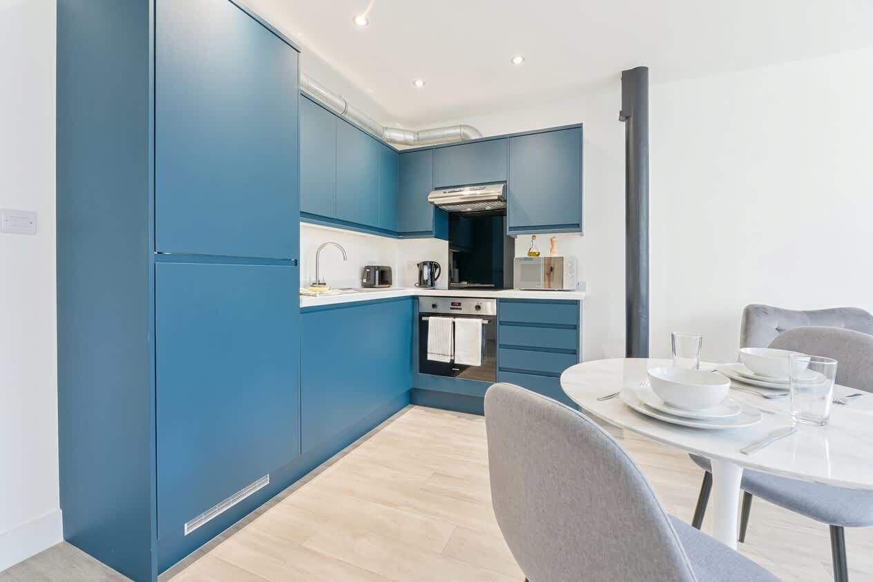 A modern kitchen with blue cabinets, a built-in oven, and a dining area with a round table and chairs.