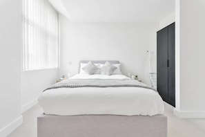 Quarto com cama, mesas de cabeceira, guarda-roupa e janela com persianas.