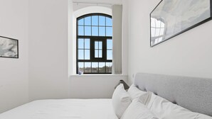 A bedroom with a large window, a bed with white bedding, and a grey headboard. - Characterful Apartment in Central Nottingham (Nottingham)