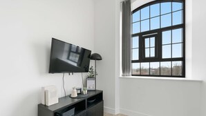 A modern living room with a flat-screen TV mounted on the wall, a dark wooden console table with decorative items, and a large window with a view of the outside. - Characterful Apartment in Central Nottingham (Nottingham)