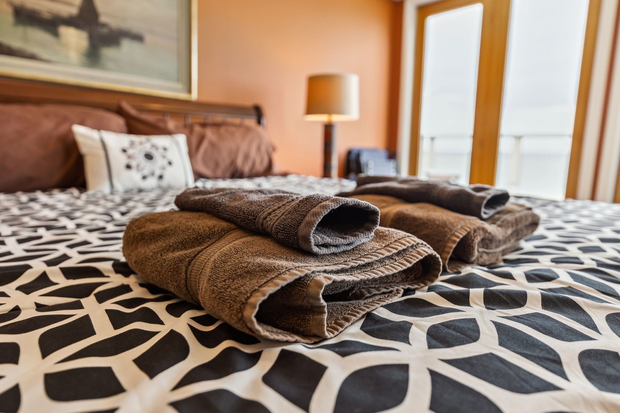 Un lit bien fait, avec une couvre-lit à motifs, une tête de lit et une lampe en arrière-plan.
