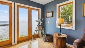 A room with large windows overlooking a body of water, a telescope, a lamp, and a wooden cabinet. - Lake Erie Getaway - Sunset Deck + Near GOTL Strip (Geneva)