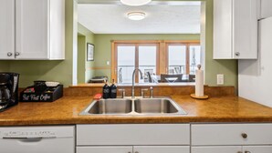 A kitchen with a double sink, white cabinets, a coffee maker, and a view of the outside through a large window. - Lake Erie Getaway - Sunset Deck + Near GOTL Strip (Geneva)