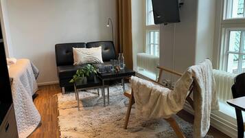 Ett vardagsrum med en svart soffa, ett soffbord, en tv som är monterad på väggen och ett stort fönster.